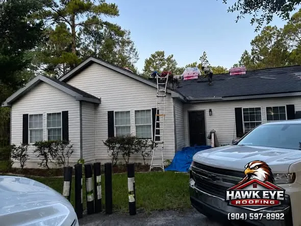 Hawk Eye Roofing crew working on a storm-damaged residential roof with a ladder set up and a tarp in place